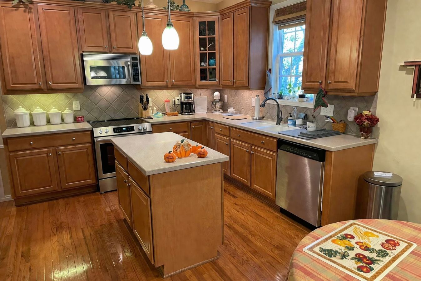Warm kitchen with wooden cabinets, central island, pendant lights, and fruit on the counter.