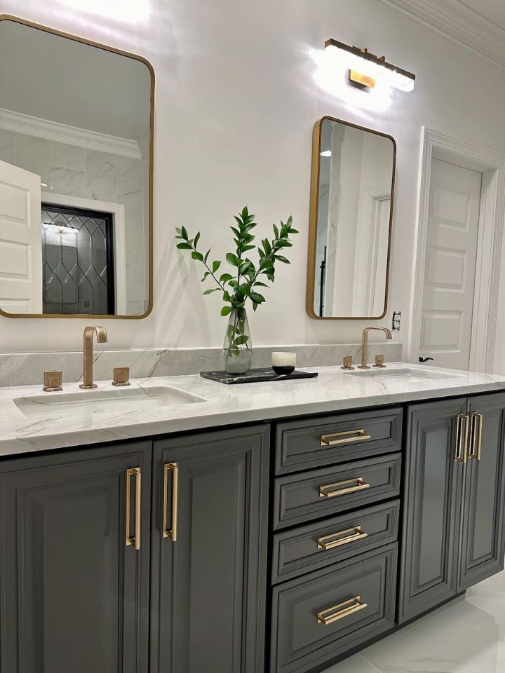 Modern bathroom vanity with dark gray cabinets, gold hardware, white countertop, and two mirrors under a wall light