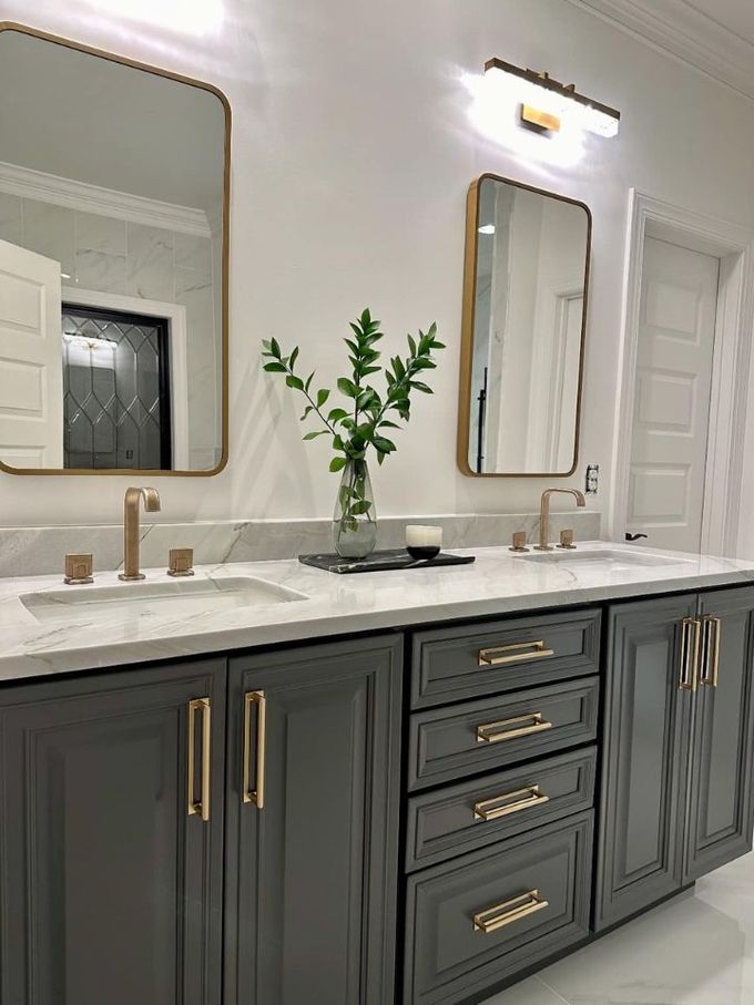Elegant bathroom vanity with dark gray cabinets, gold hardware, marble countertop, and wall mirrors.