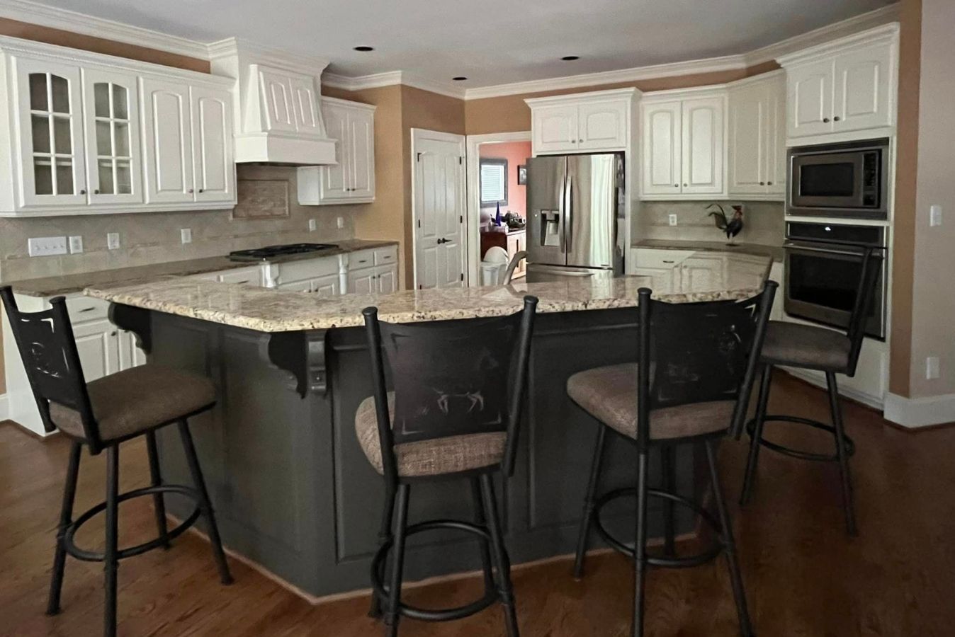 Bright kitchen with granite island, white cabinets, stainless appliances, and three black stools