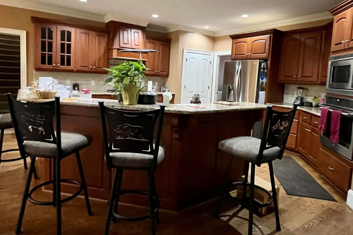 Spacious kitchen with wooden cabinets, island seating, and stainless steel appliances, warmly lit at night