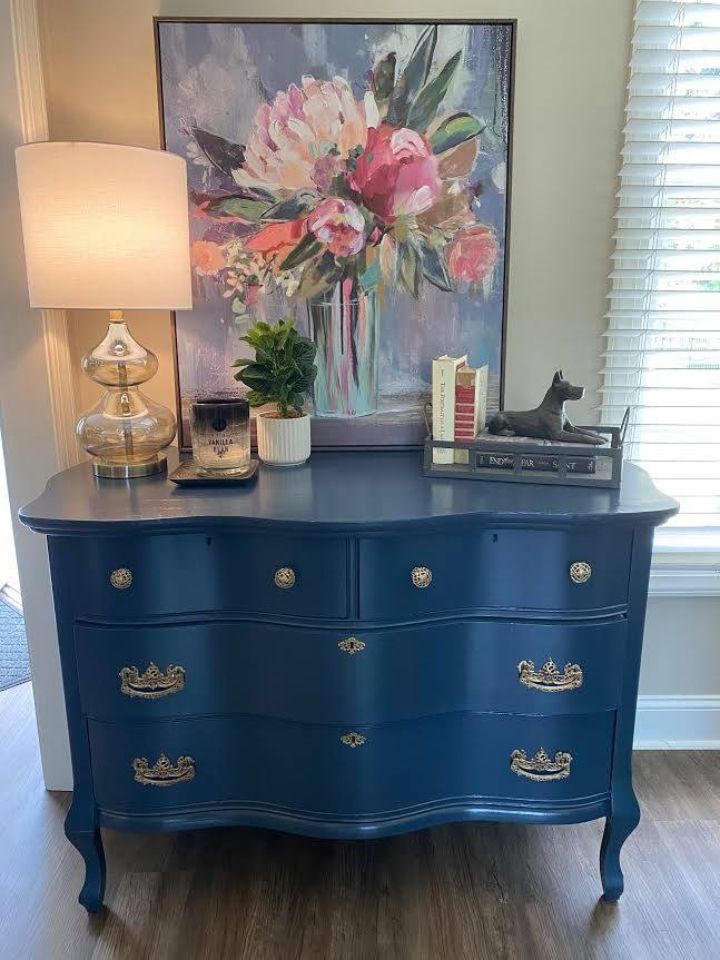 Blue dresser with lamp, floral painting, and small decor items in a home interior