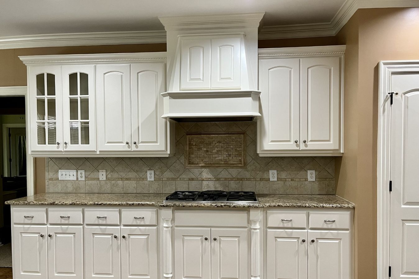White kitchen with granite countertops, tiled backsplash, built-in cabinets, and a range hood above the stove.
