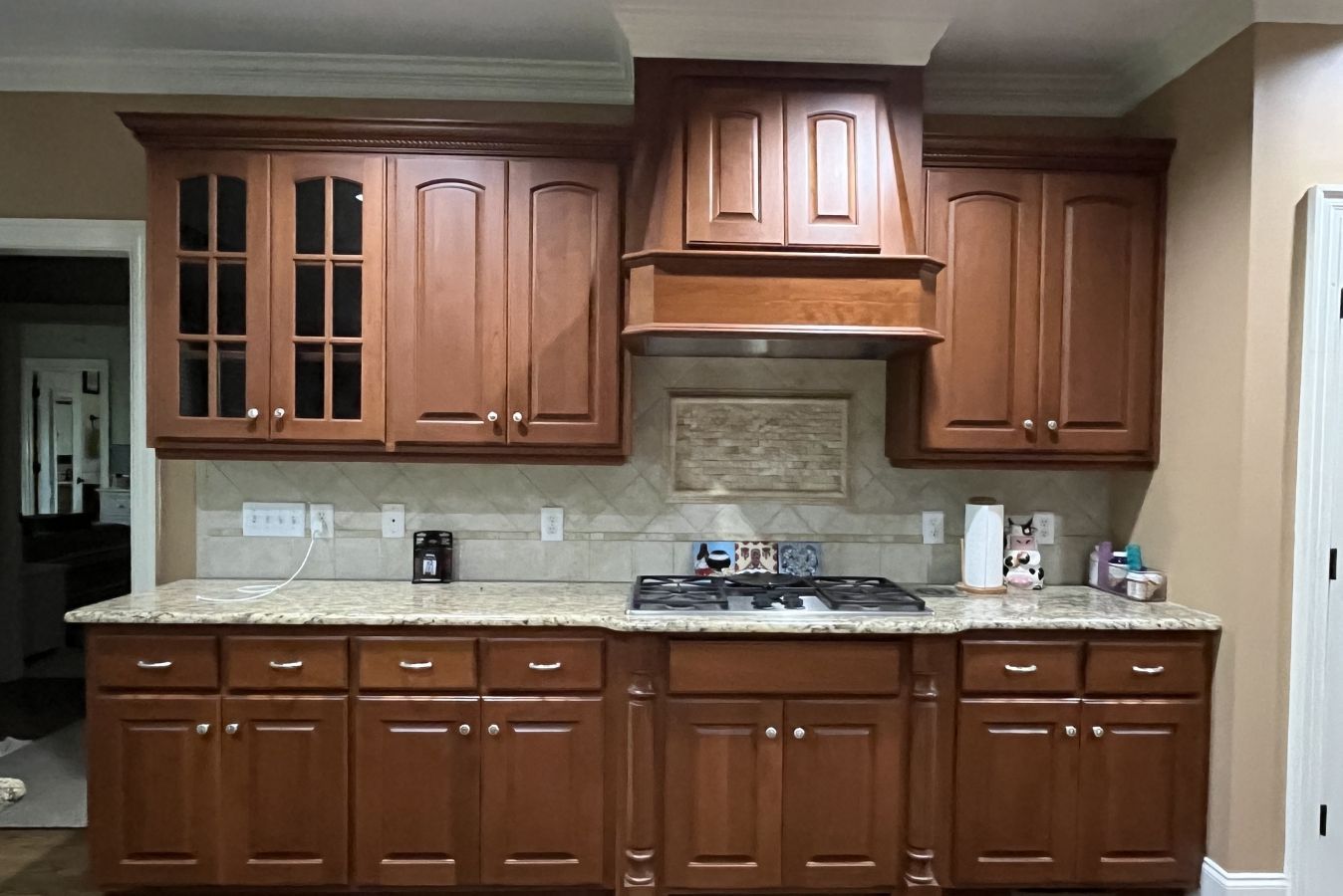 Wooden kitchen cabinets and counters with a central range hood and beige backsplash.
