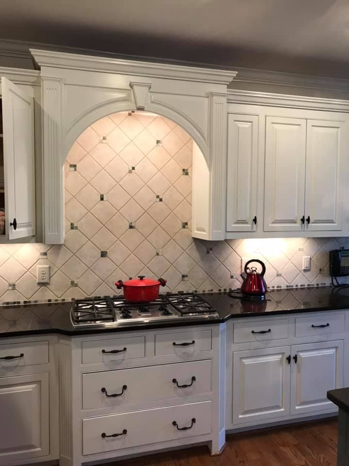 White kitchen with arched tile backsplash, black countertop, gas range, and red pot.