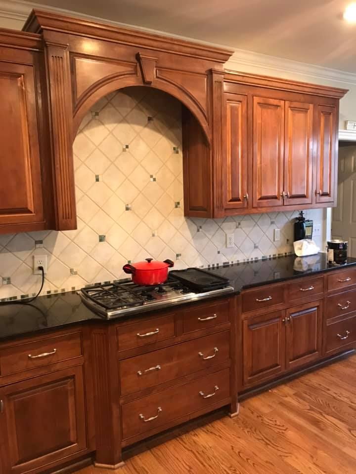 Wooden kitchen cabinets and black countertop with red pot on a gas stove and tiled backsplash.