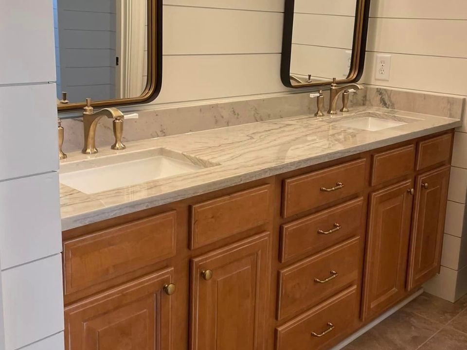 Bathroom vanity with double sinks, marble countertop, wood cabinets, and wall mirrors