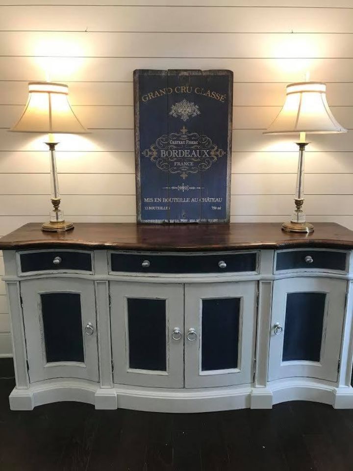 White buffet cabinet with lamps and a decorative blue sign against a cream wall.