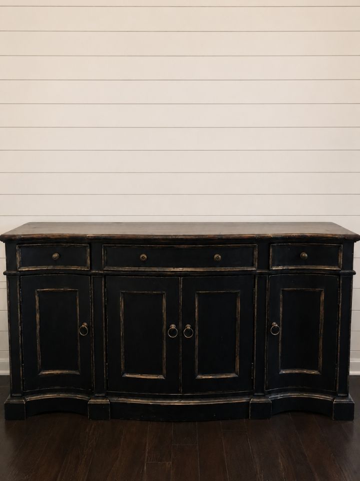 Black wooden sideboard cabinet with drawers and cabinet doors against a white shiplap wall
