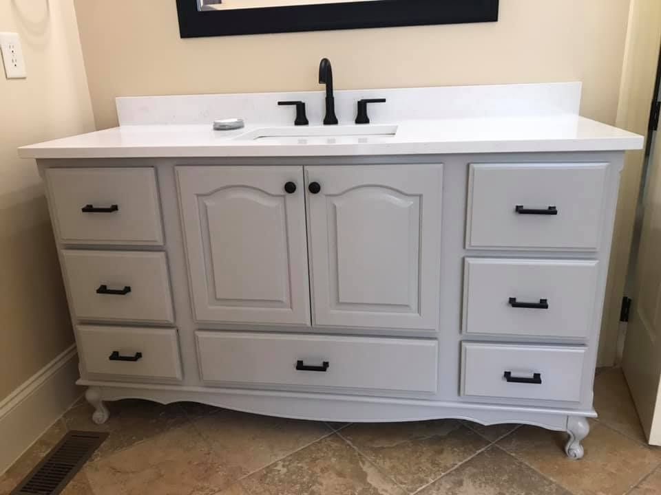 White bathroom vanity cabinet with black faucet and sink, centered against a light wall.