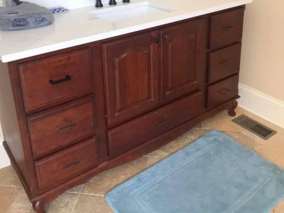 Bathroom vanity with dark wood cabinets, white countertop, blue bath mat, and floor vent