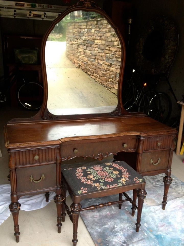 Antique wooden vanity with mirror and stool in a dim room by a stone wall outside opening