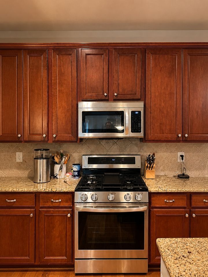 Kitchen with cherry wood cabinets, stainless steel microwave and gas range, and beige granite countertops.