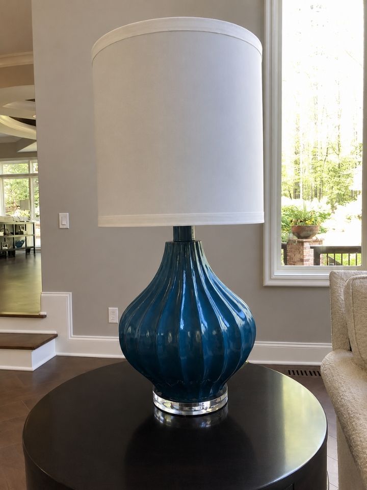 Blue glass table lamp with white shade on a round dark wood table in a living room