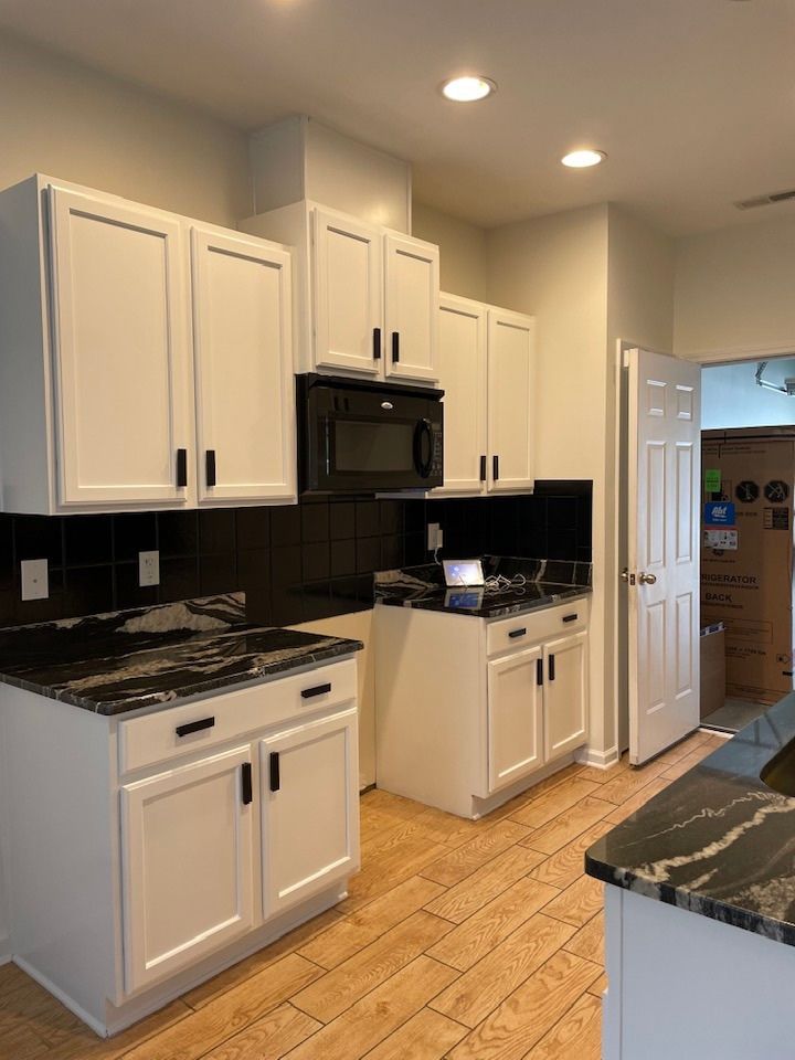 Modern white kitchen with black countertops, stainless appliances, and tan tile floor