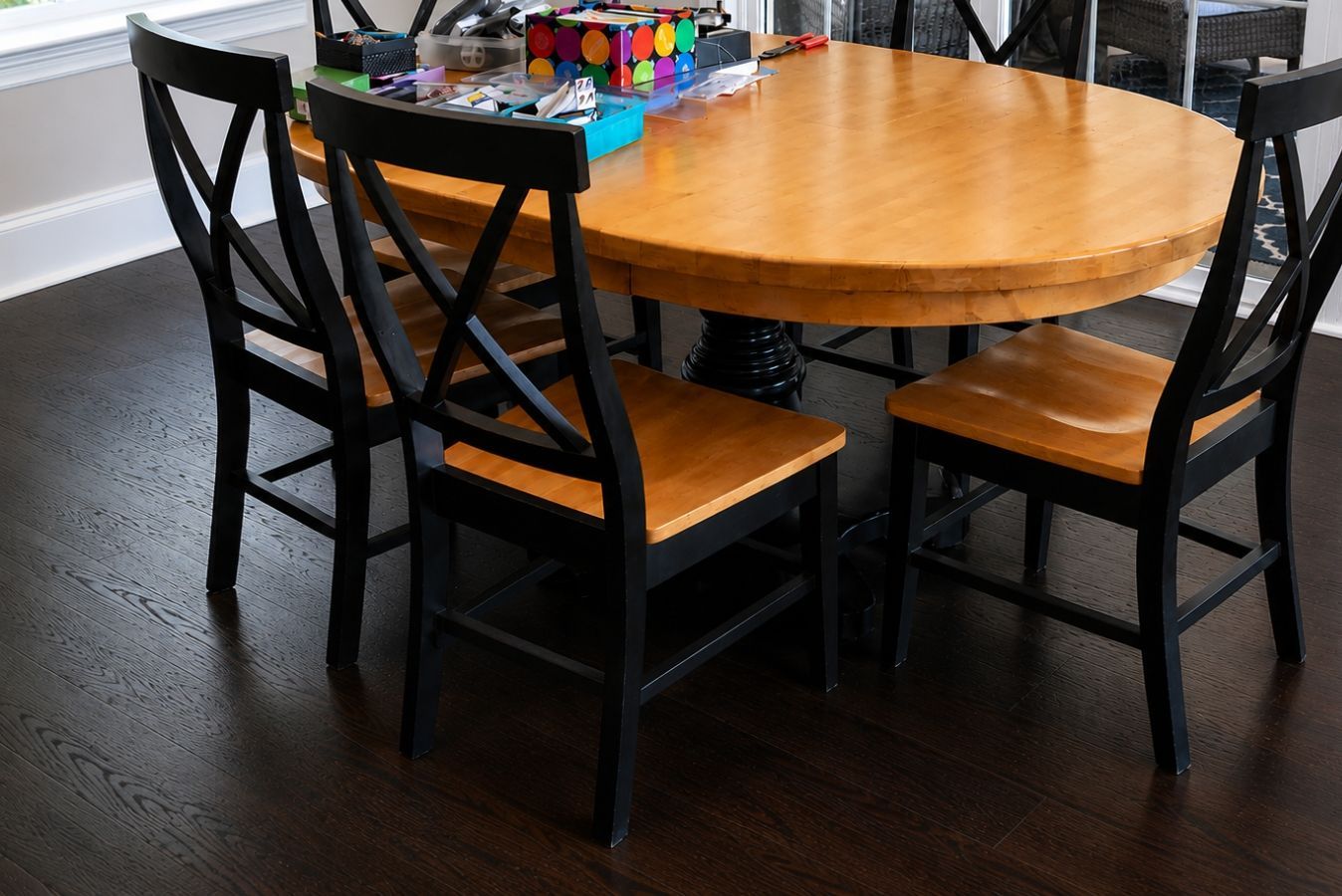 Round wooden dining table with black chairs and a tray of colorful markers on top