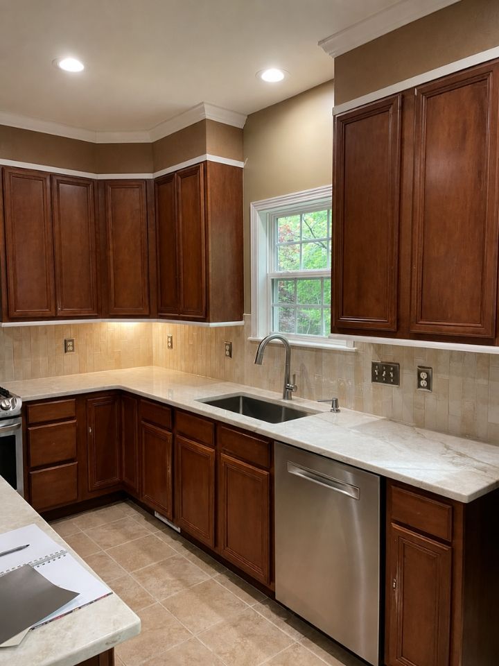 Modern kitchen with dark wood cabinets, beige tile backsplash, white counters, and a window above the sink.