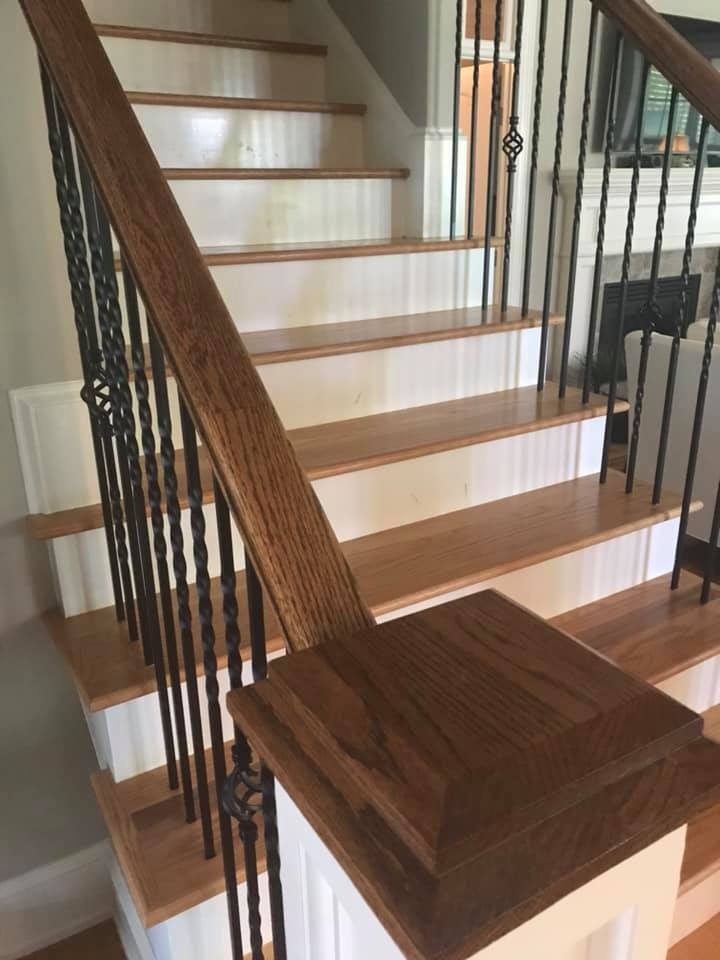 Wood staircase with white risers, wooden treads, black metal balusters, and a wooden newel post.