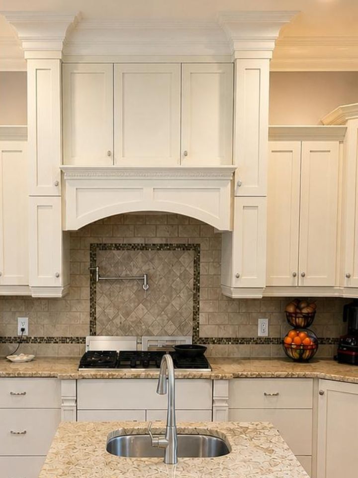 Bright kitchen with white cabinets, central island sink, and tiled backsplash around a stove niche