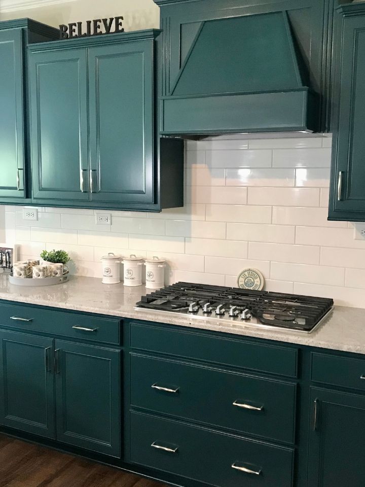 Teal kitchen with white backsplash, gas stove, and cabinets above and below countertops