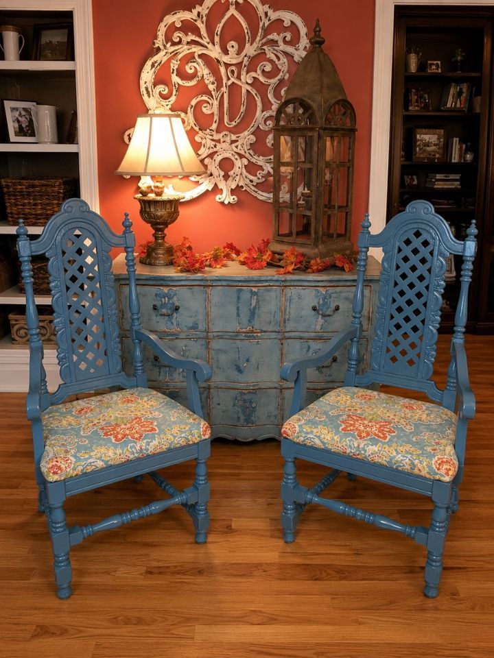 Two blue carved chairs in front of a blue dresser with a lamp, orange wall decor, and wooden floor