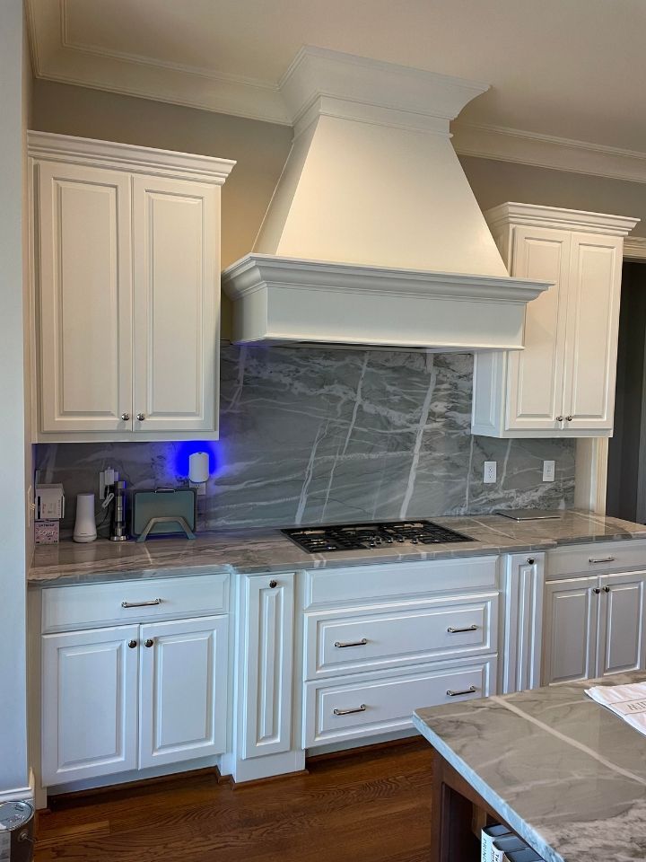 White kitchen with marble-look backsplash, cabinets, range hood, and granite island countertop.