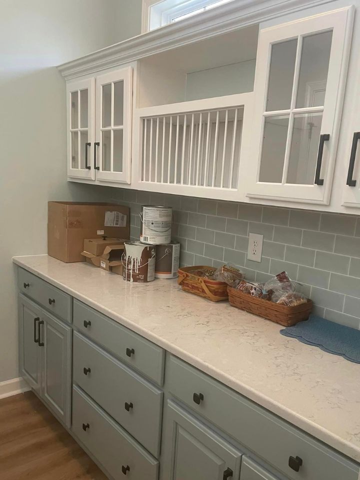 White and sage kitchen with glass-front cabinets, subway tile backsplash, and countertop decor