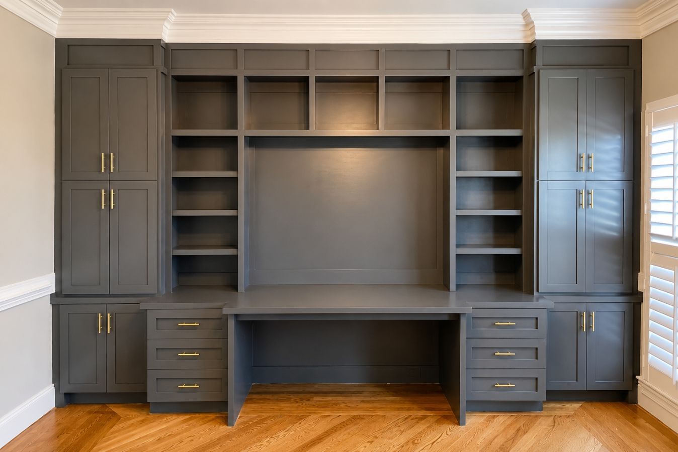 Gray built-in wall unit with shelves, cabinets, and desk in a room with hardwood floors.