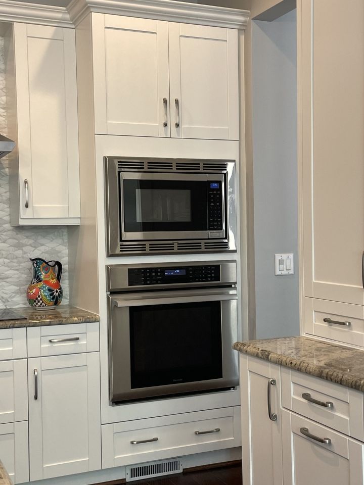 Built-in stainless steel oven and microwave in a white kitchen with marble countertops