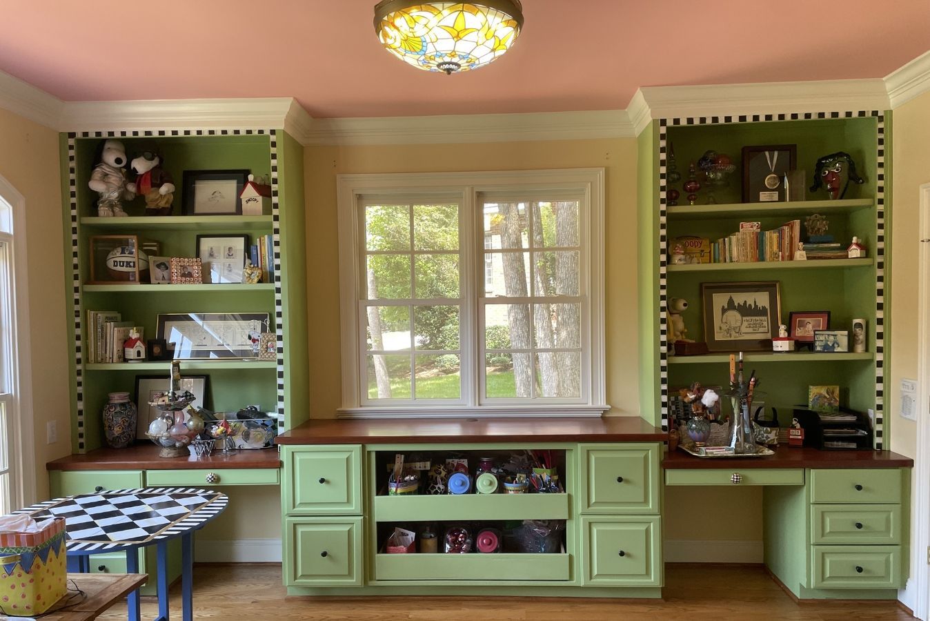 Pink playroom with mint-green built-ins, toys, and a centered window above a cabinet