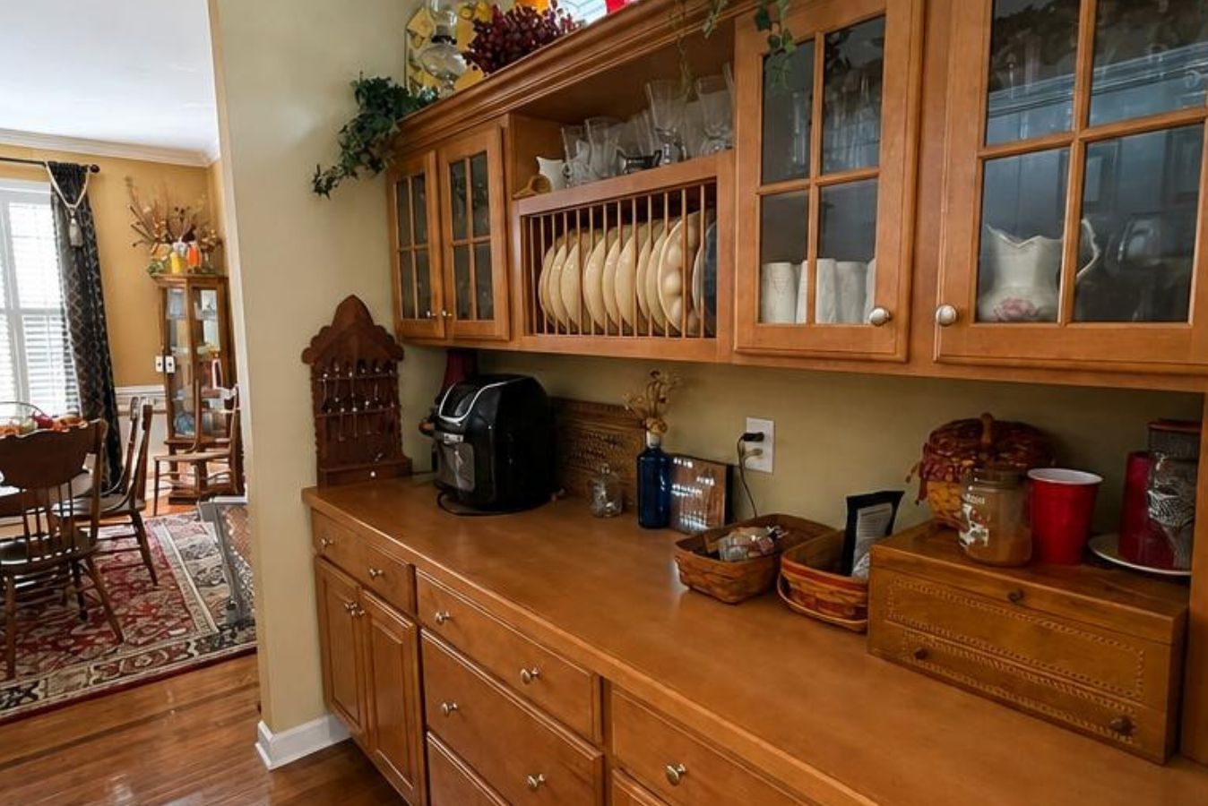 Wooden sideboard with glass-front cabinets, countertop decor, and a coffee maker in a warm dining room
