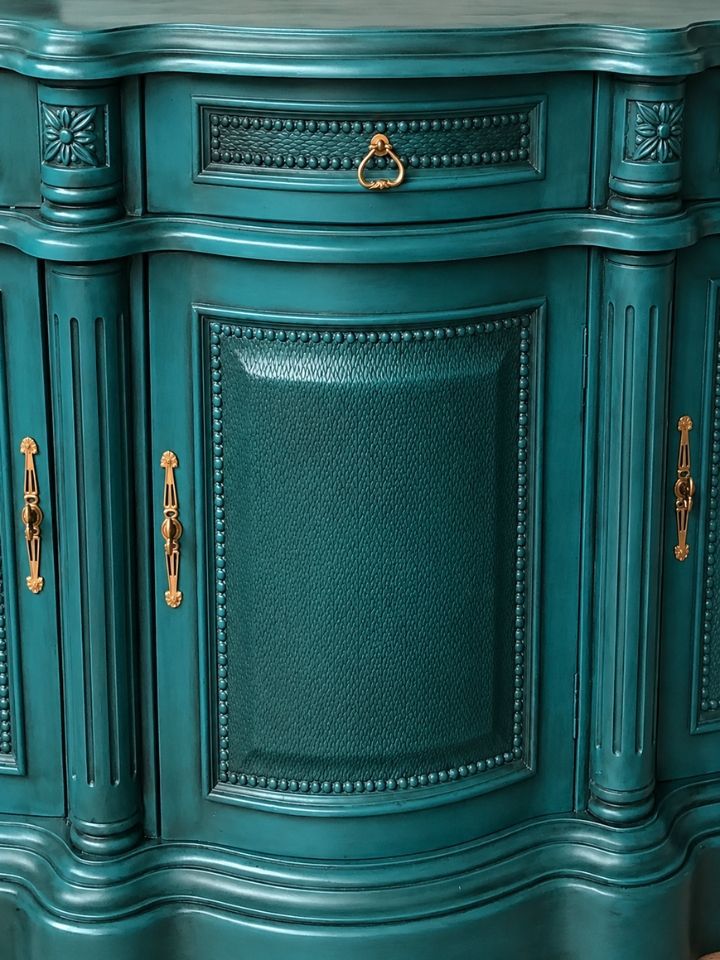 Teal painted wooden cabinet with ornate trim and gold handles