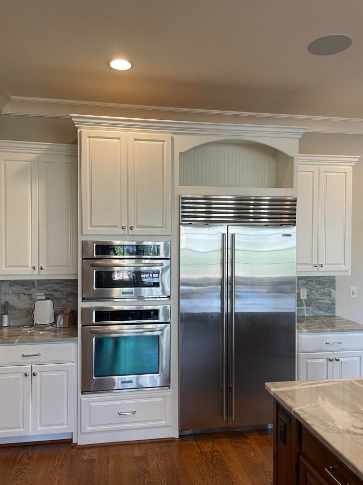 Bright white kitchen with stainless steel double refrigerator, wall ovens, and marble island countertop.
