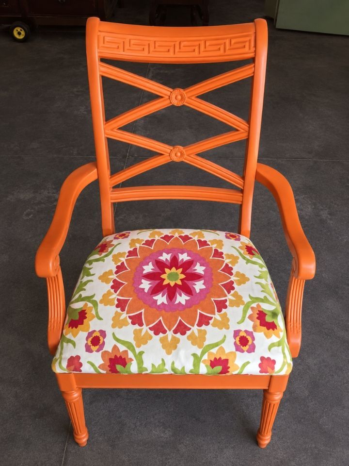 Orange wooden chair with floral seat cushion against a dark background