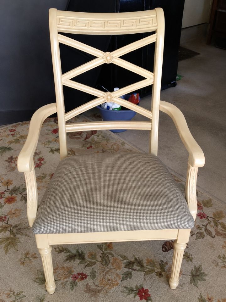 Beige upholstered armchair with carved wood frame and X-shaped backrest on a floral rug.