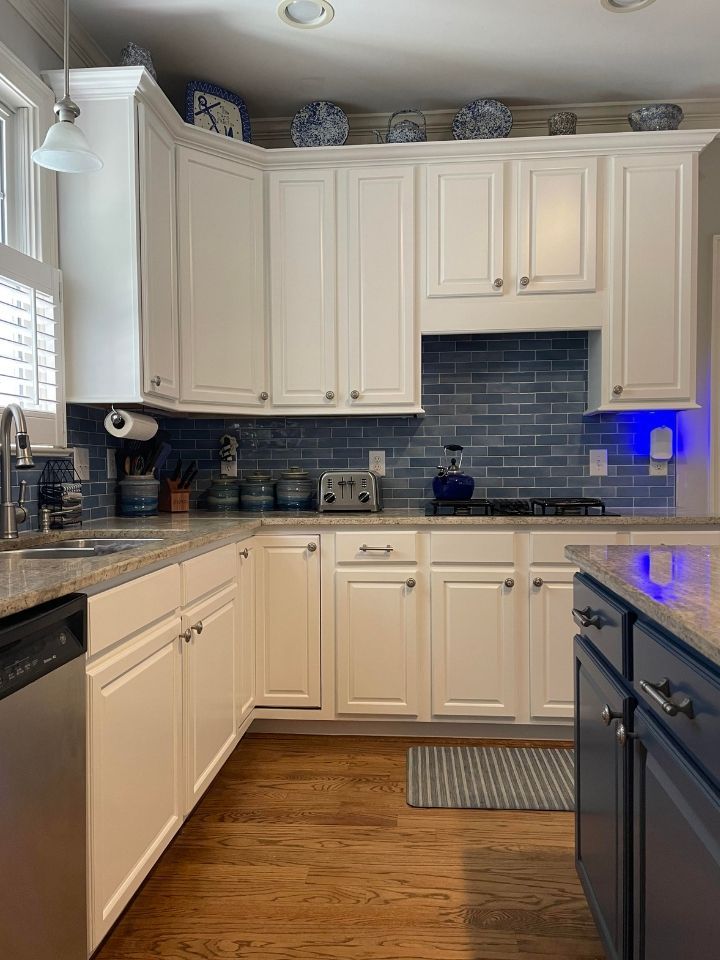 Bright white kitchen with blue tile backsplash, black appliances, and hardwood floor