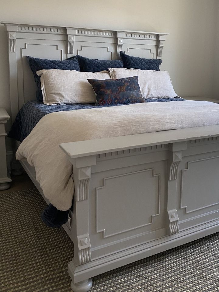 White upholstered bed with carved headboard, layered pillows, and white bedding in a neutral bedroom