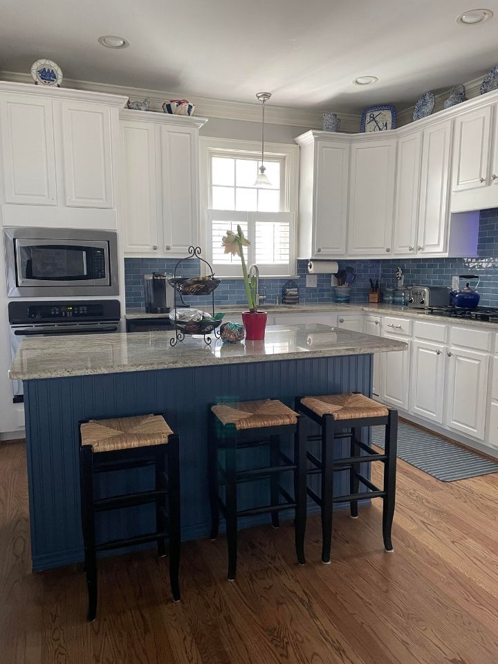 Bright kitchen with white cabinets, blue island base, granite counters, and three stools under the island.