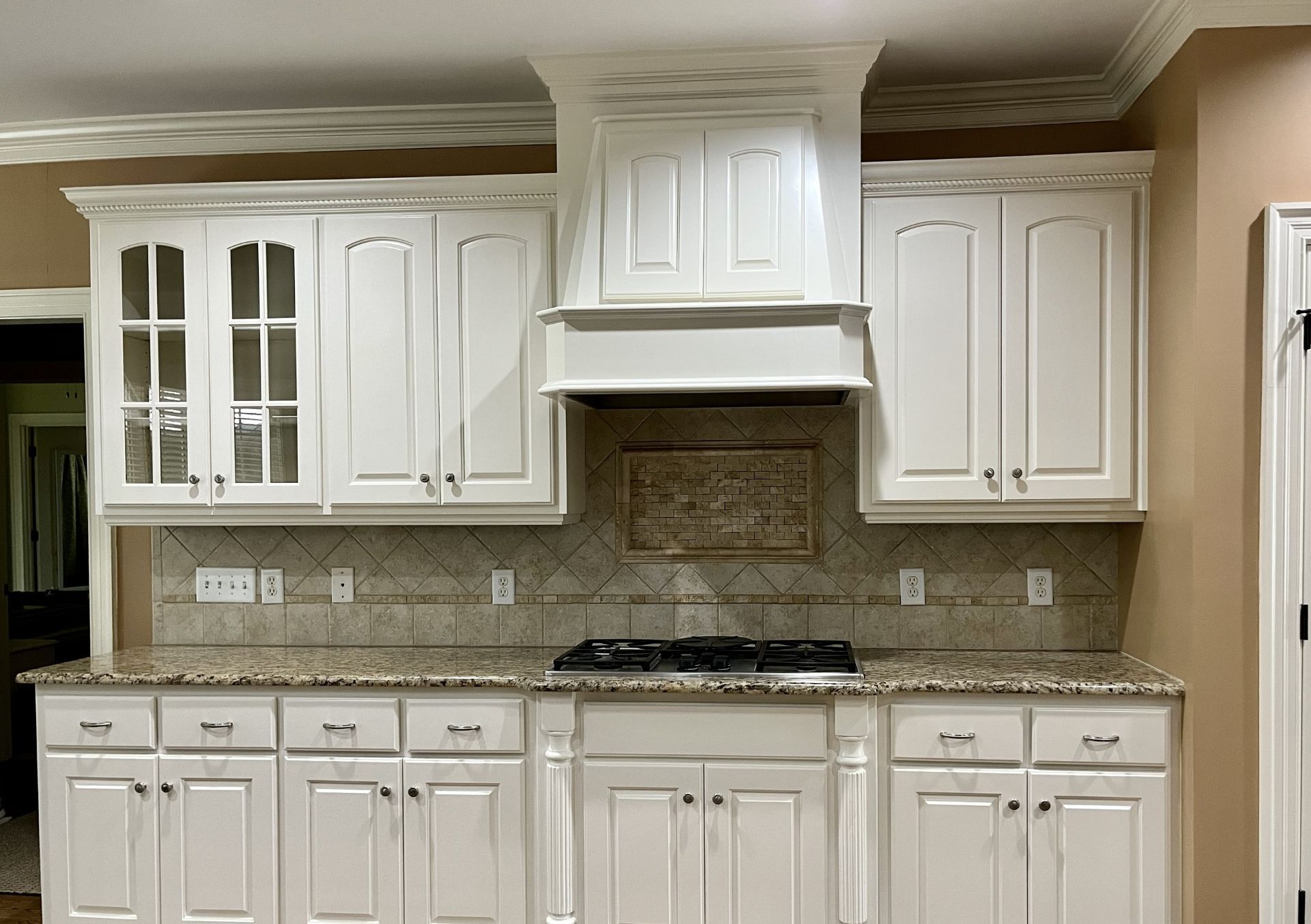 White kitchen with cream cabinets, granite countertop, tiled backsplash, and stainless gas range.