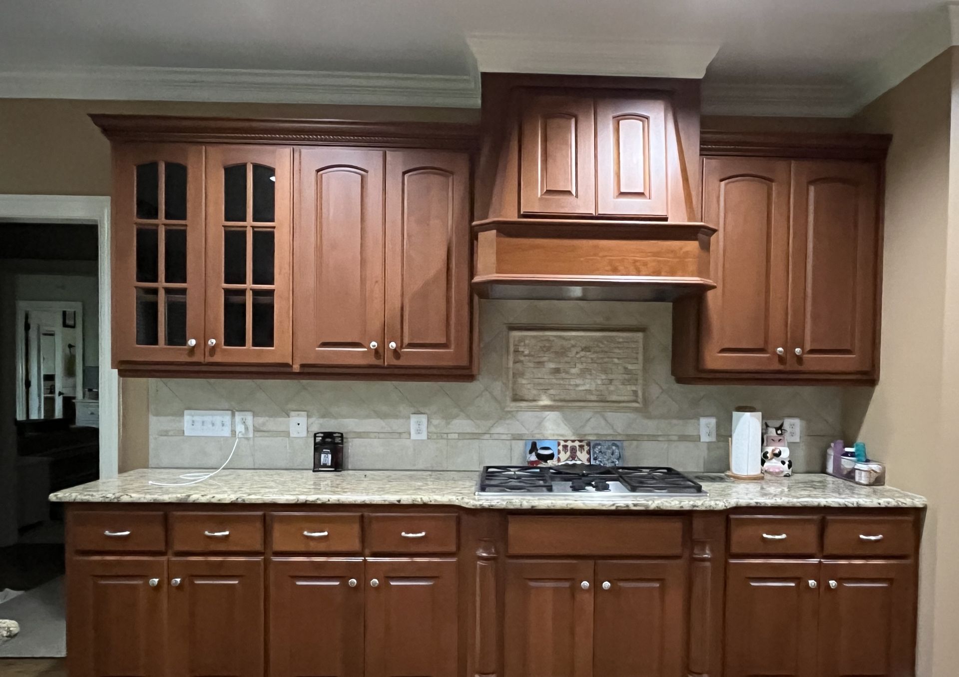 Wooden kitchen cabinets with granite countertops, stove, and tile backsplash under a range hood.