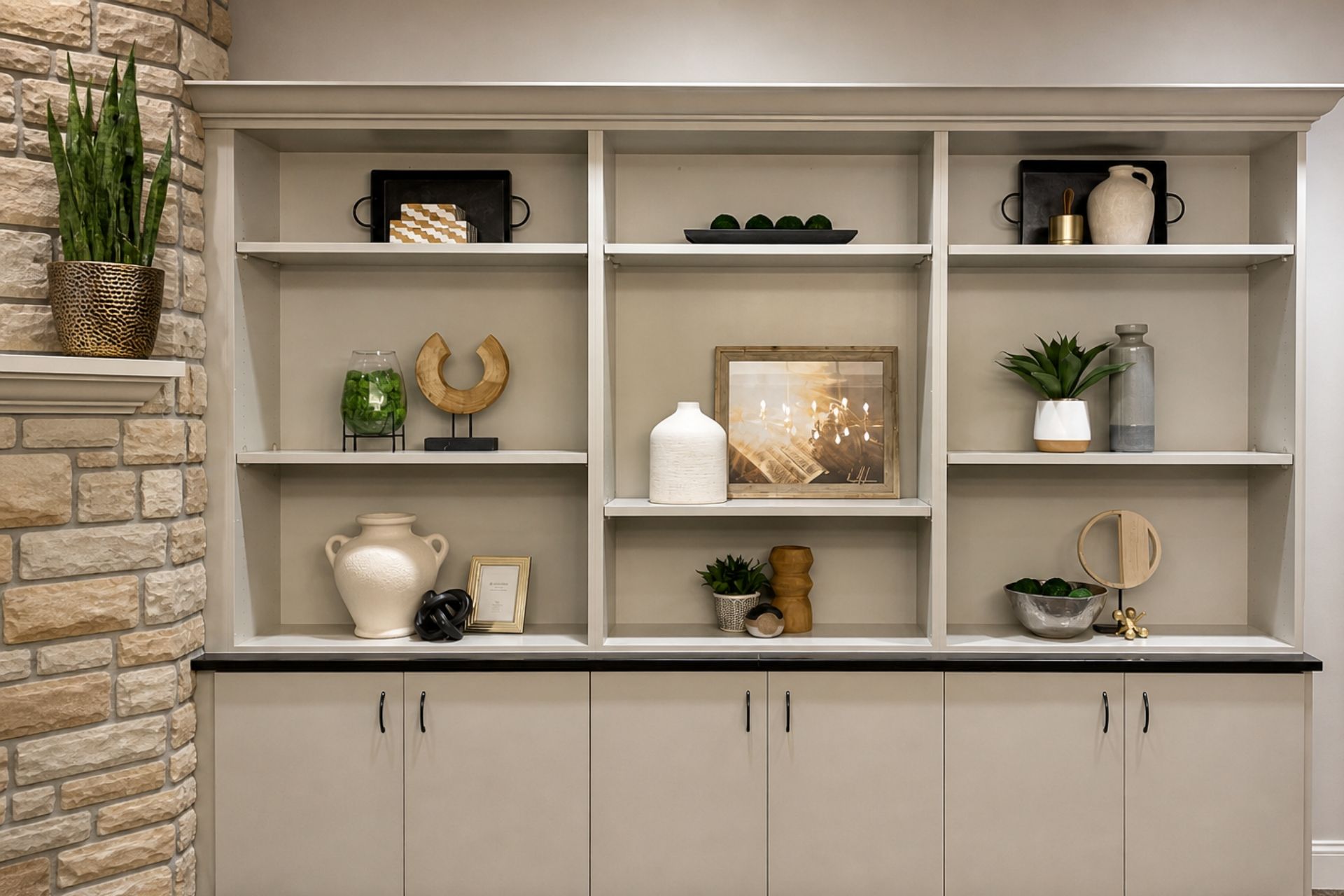 Built-in living room shelving with decor, plants, and cabinets, featuring neutral tones and stone accent wall