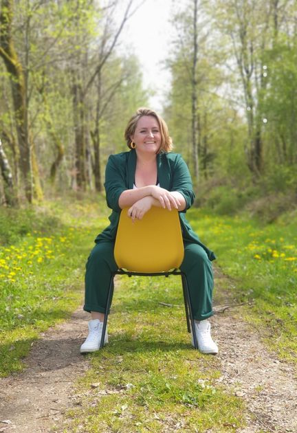 Patricia Keizer zit op een gele stoel op een bospad, gekleed in een groen pak en witte sportschoenen.