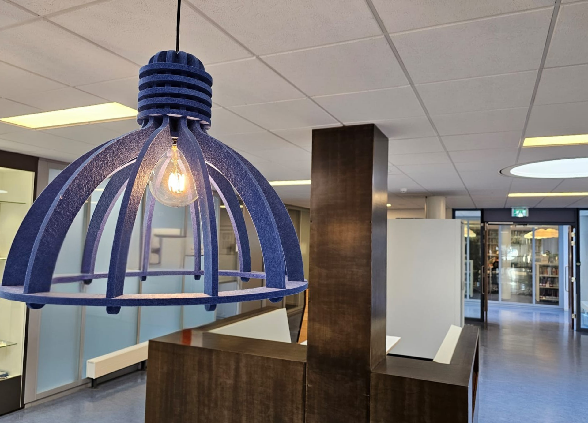 Blauwe hanglamp boven een informeel treincoupé met houten scheidingswanden en een systeemplafond