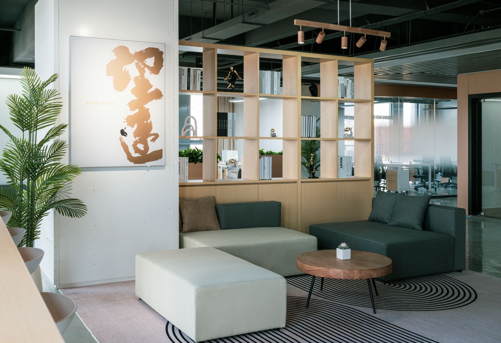 Moderne kantoorlounge met zachte zitmeubelen, houten kast, een potplant en abstracte muurdecoratie.