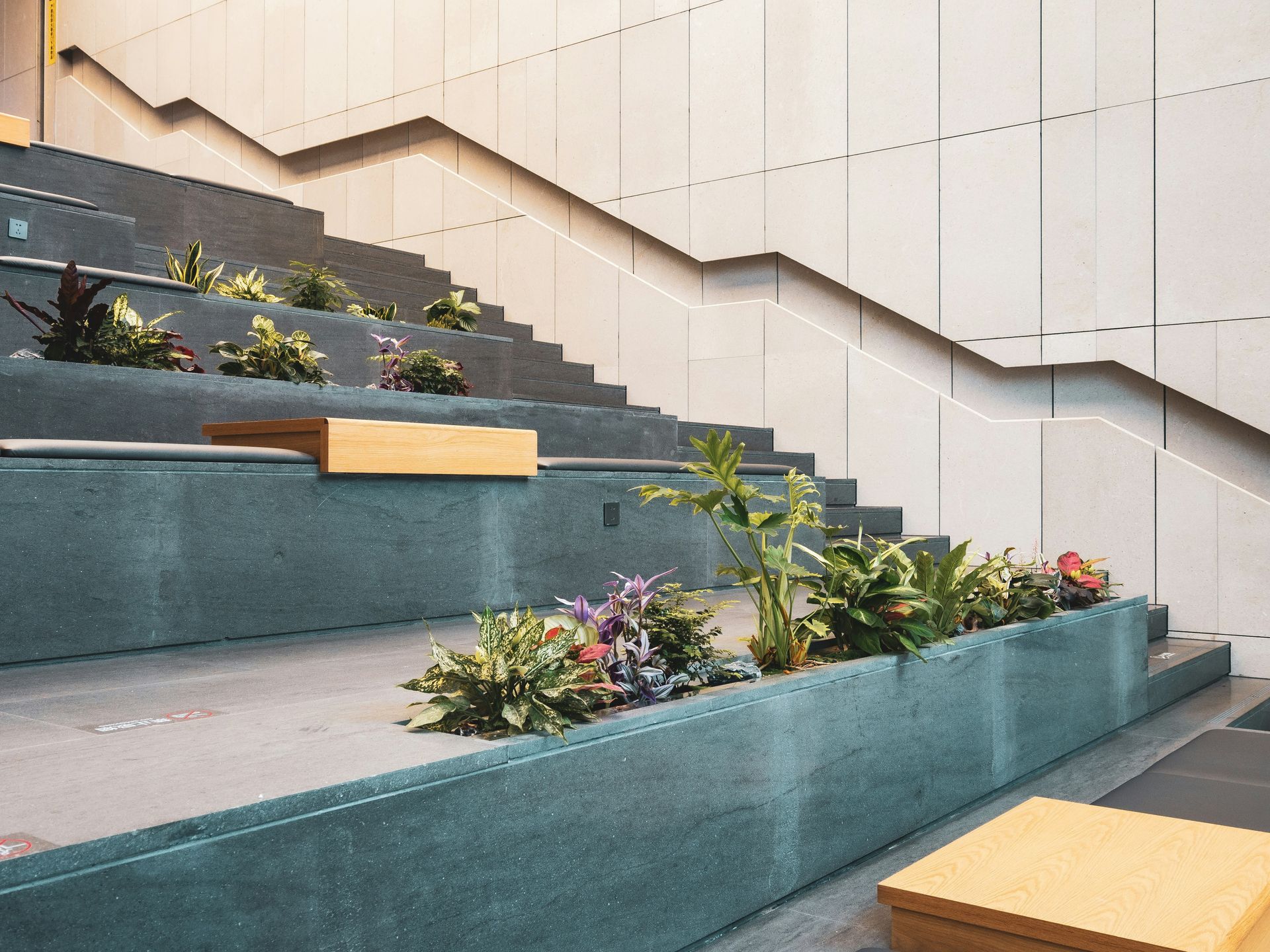 Moderne, trapsgewijs aangelegde plantenbak met turquoise bankjes, groene planten en gele blokken langs een trap.