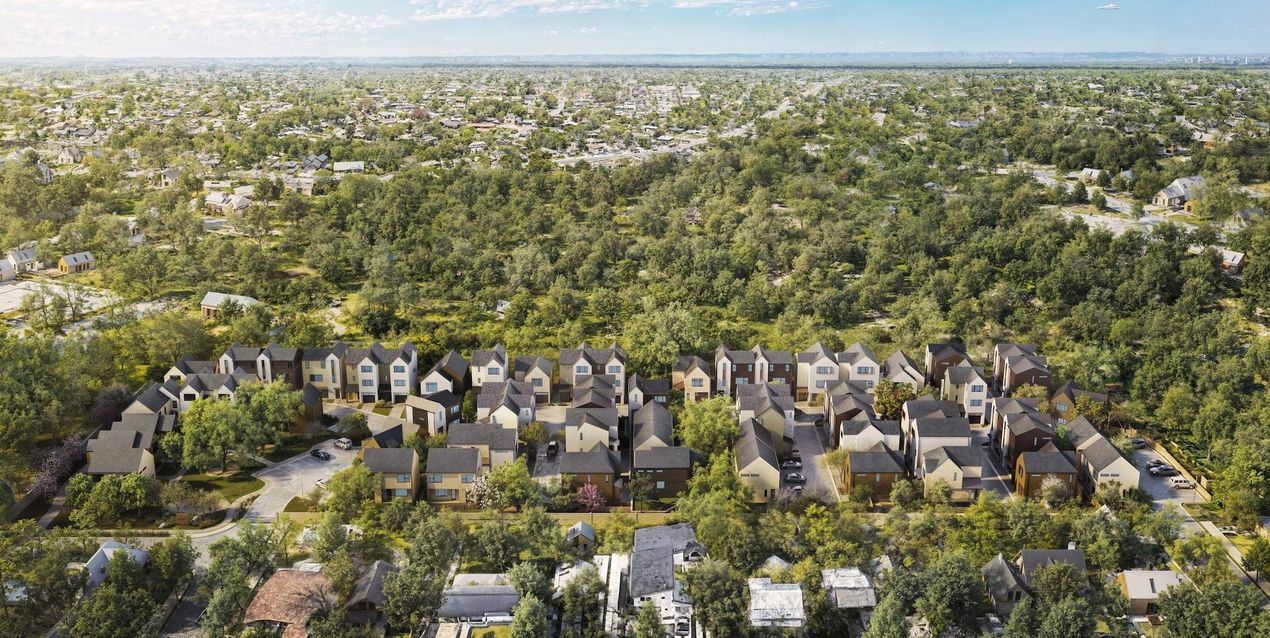 Aerial view of a residential neighborhood surrounded by dense green trees. Homes have various colors and styles.
