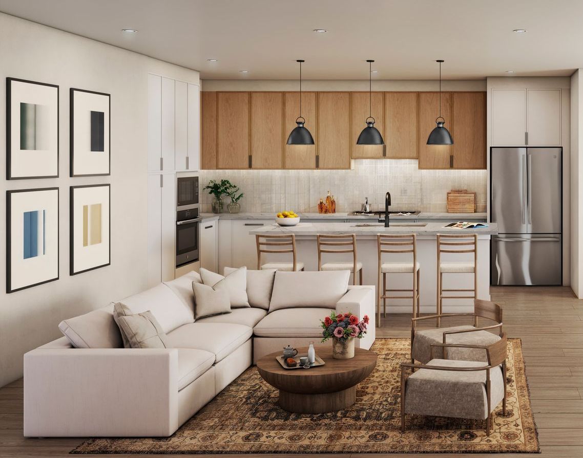 Open-concept living space with a white sectional sofa, kitchen with light wood cabinets, and dining island.