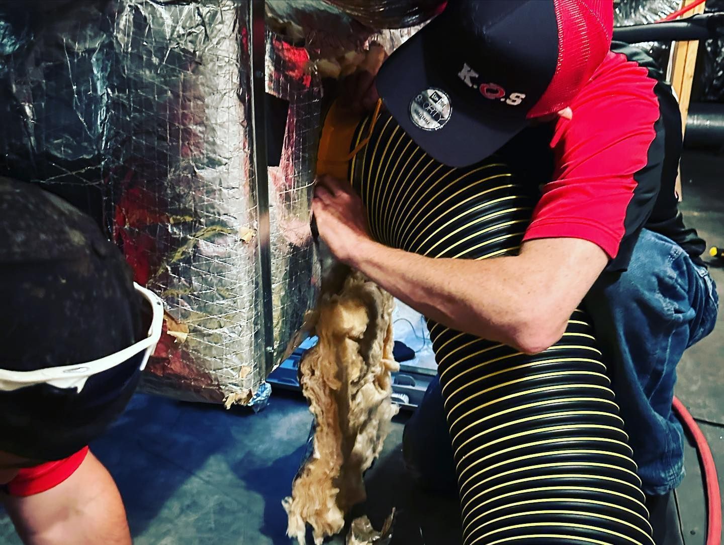 a man wearing a red shirt and a black hat is cleaning a duct with a vacuum hose .