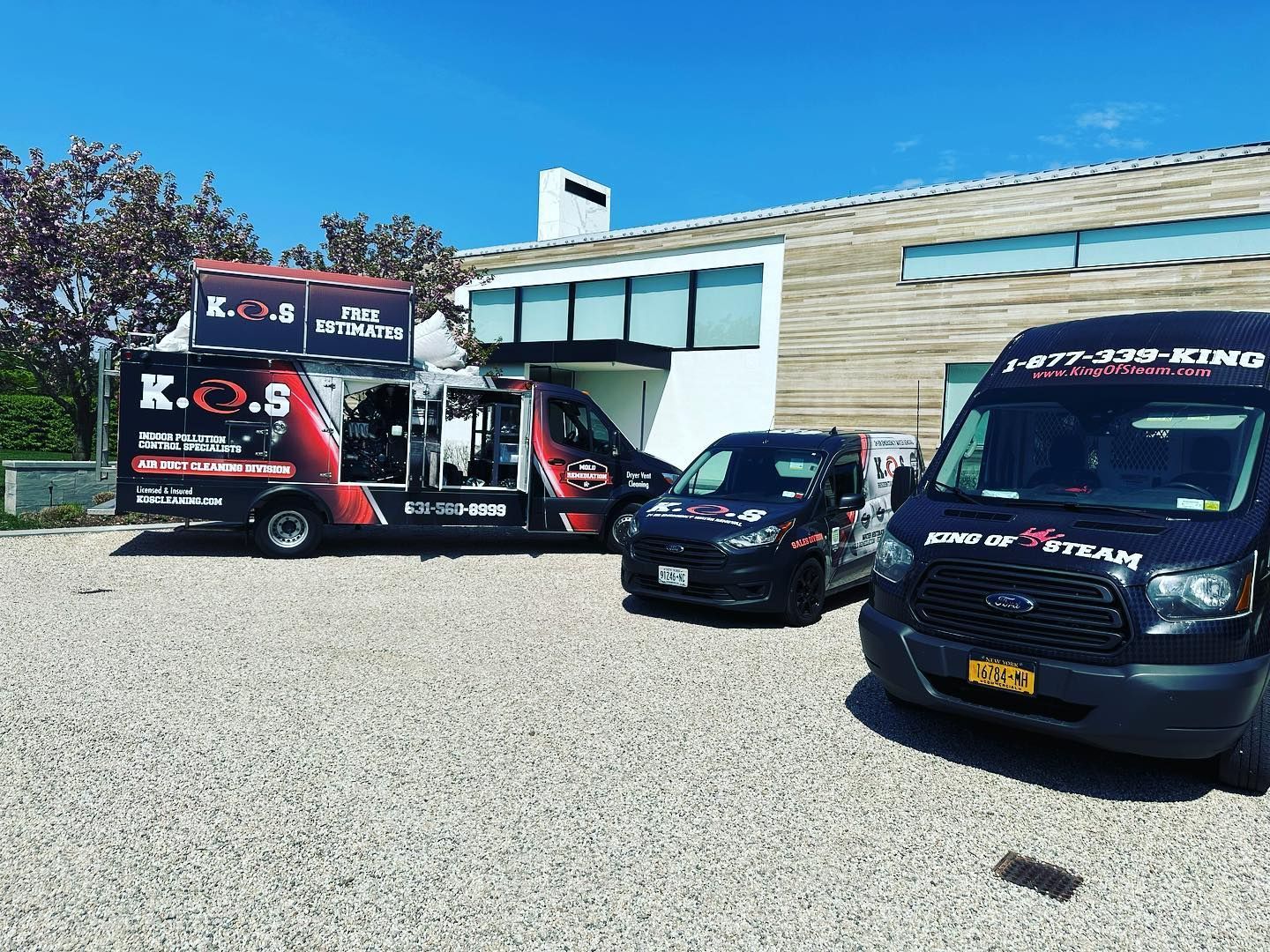 three vans are parked in a gravel lot in front of a building .