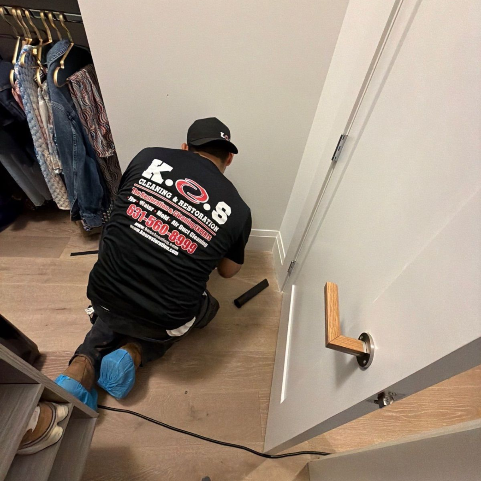 Person kneeling on a closet floor, using a tool near a white wall and open shelving.